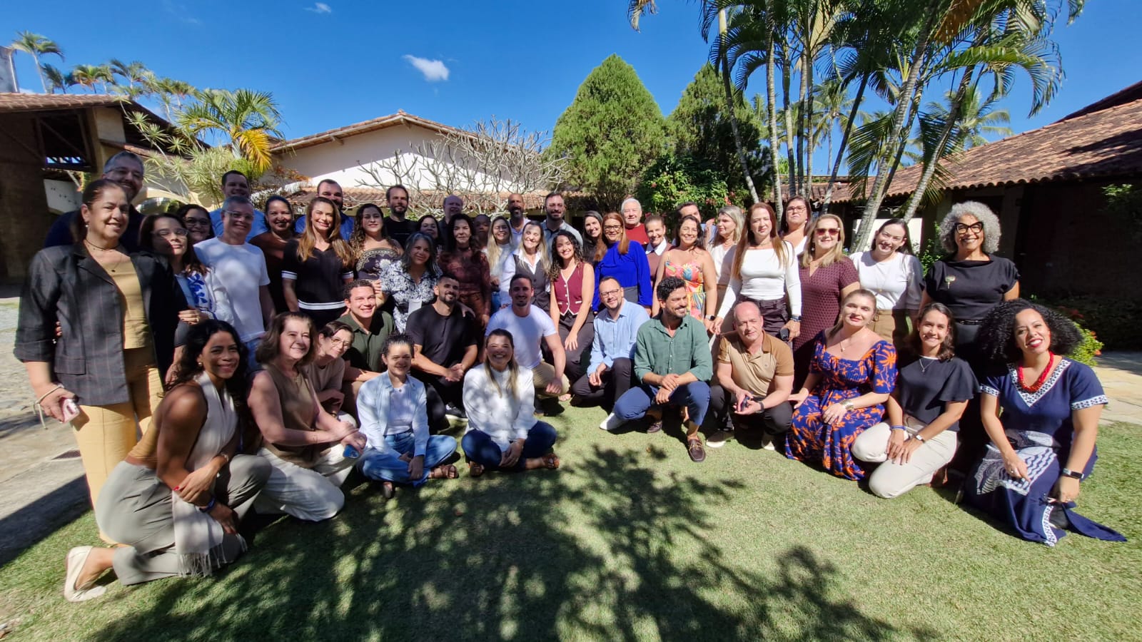 Fotografia de um grupo com cerca de 45 pessoas reunidas em um jardim ao ar livre, posando para uma foto. O grupo está distribuído em três fileiras.